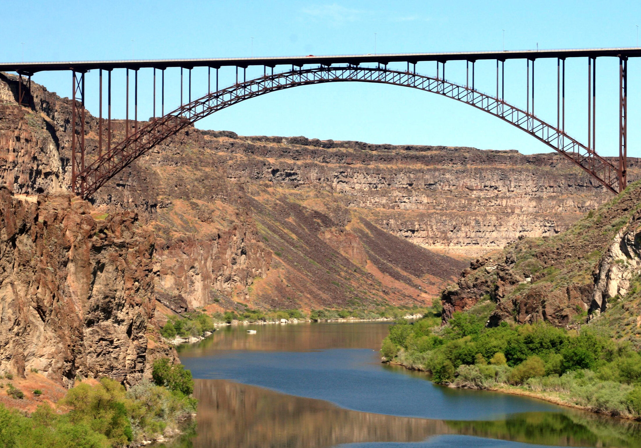 A scenic bridge spans a river, surrounded by lush greenery and a clear blue sky